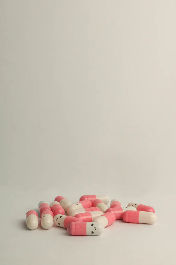 Pink and white capsules with smiley faces and heart shaped eyes laying on off-white table.