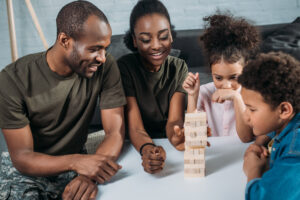 Black Family with two children playing wooden block game in living room. 